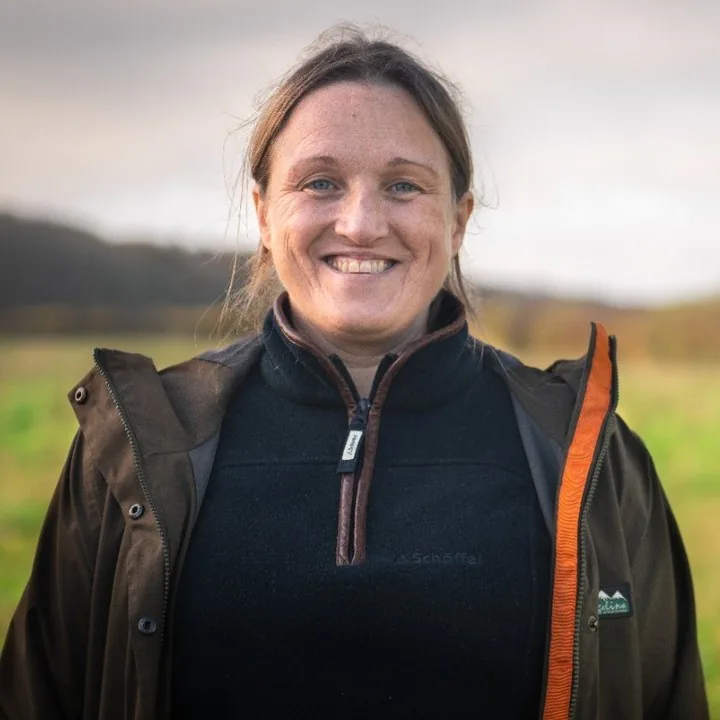 Clare Hill standing in a field at Planton Court Farm, in a waxed jacket, with the Shropshire hills behind her.